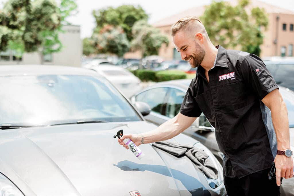 A man smiling while spraying Torque Detail Ceramic Spray to his car.