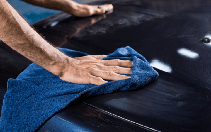 man wiping the hood of a black car