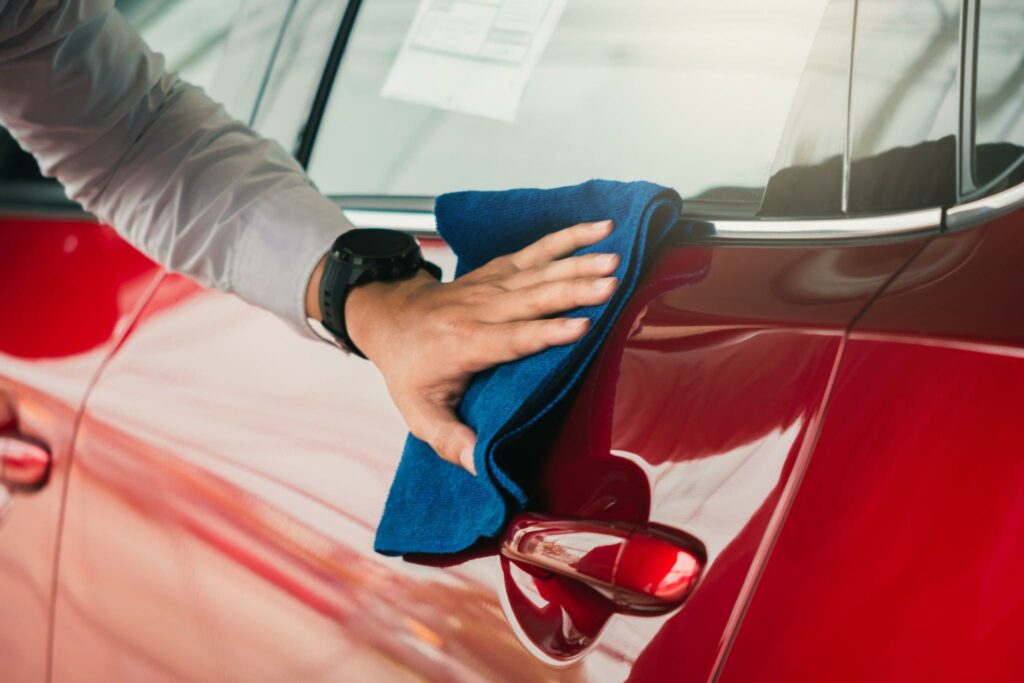 A person using a microfiber towel to remove acid rain residue from a car's paint