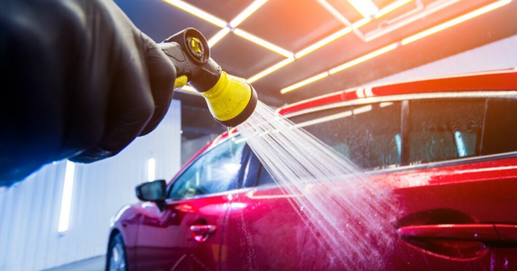 The image depicts a car being washed with a pressure washer, highlighting the significance of regular car washes in protecting the vehicle's paint from acid rain damage