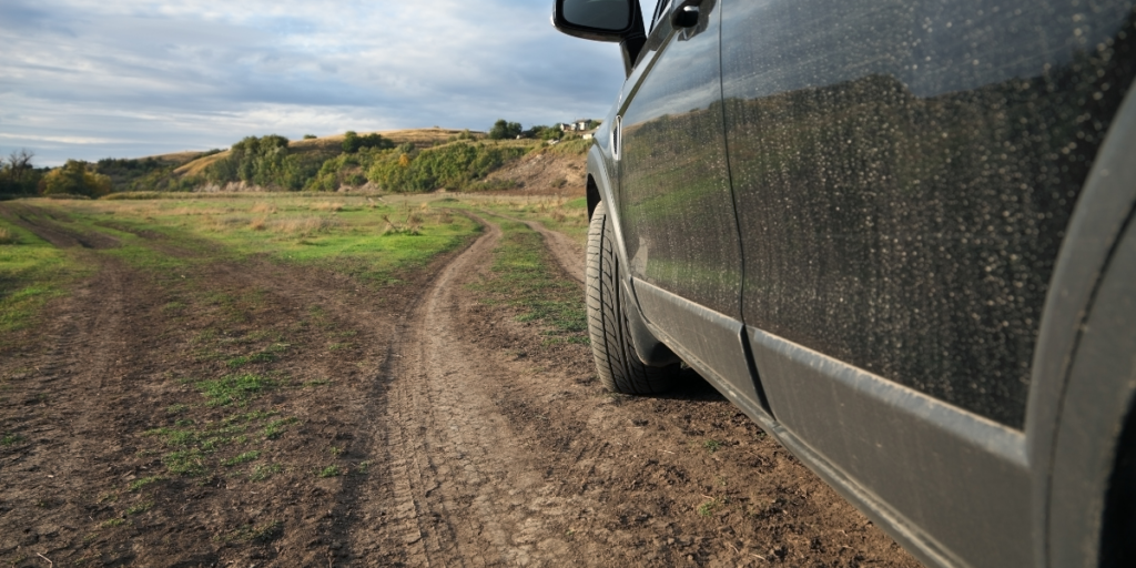 A black car stands in the middle of a countryside setting, covered in dirt and dust.