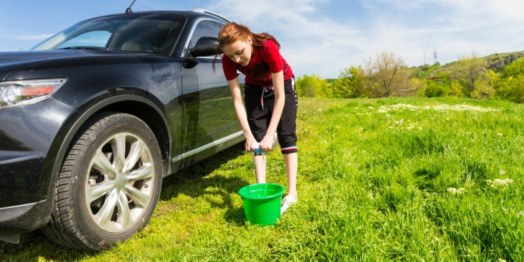 A young woman diligently caring for her black car in peaceful surroundings, gracefully rinsing its surface with water. 