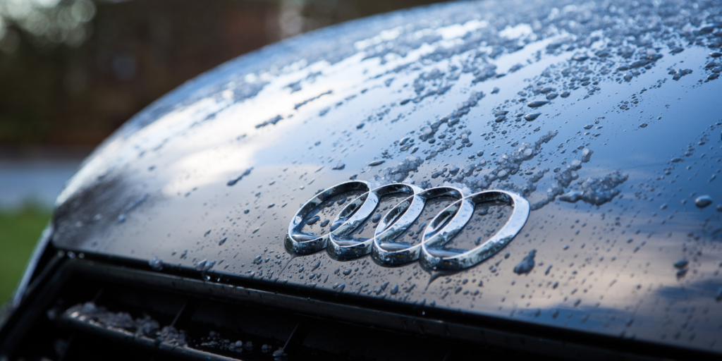 The image captures a front view of a sleek black car covered with raindrops and water spots