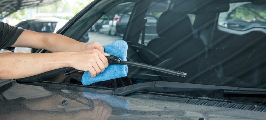 Professional detailer paying close attention to forgotten wiper cowls during a car cleaning session.