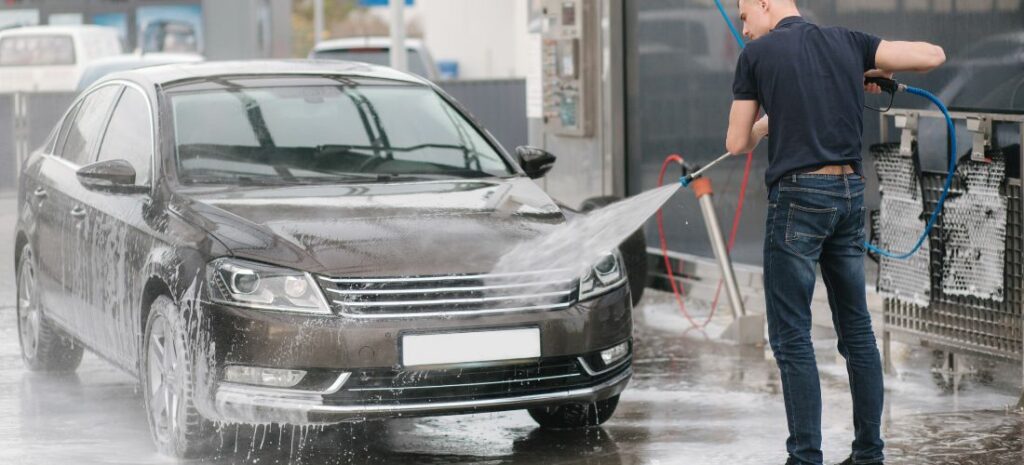 A man pressure washing a black car, restoring the car's beauty and removing sticky material.