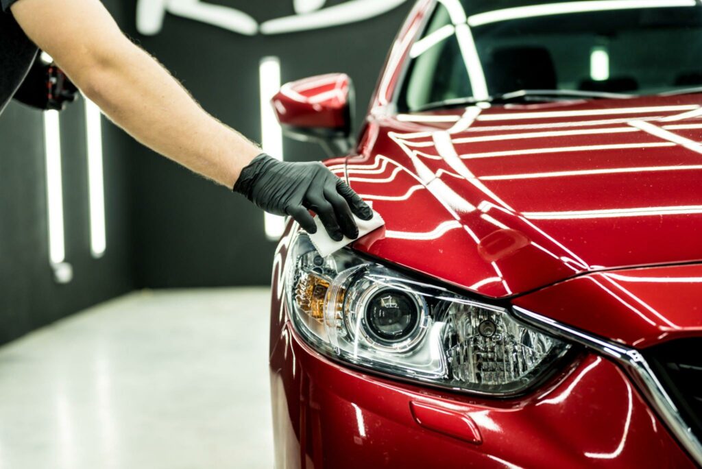 Car service worker applying a coating on a red car.