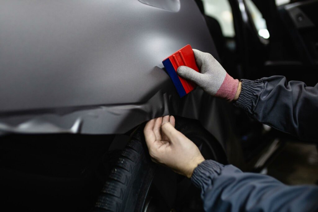 Hand of a car wrapping specialist smoothing the vinyl foil or film on car by using squeegee.