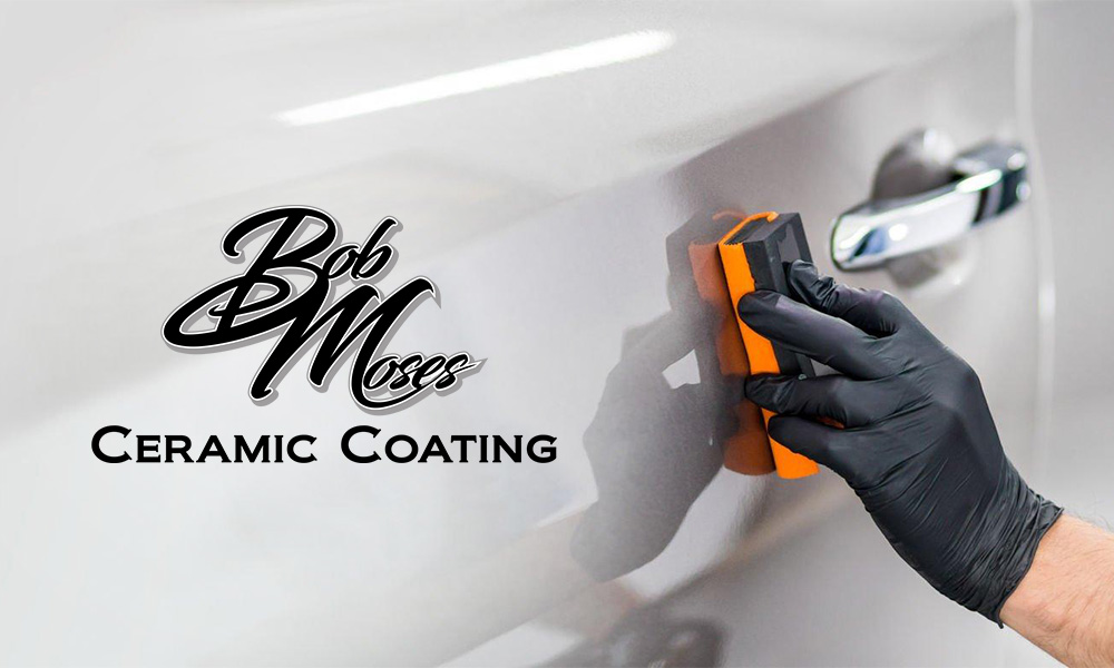 Close up view of a man's hand applying a protective coating to a silver car with Bob Moses Ceramic Coating logo at the left side.