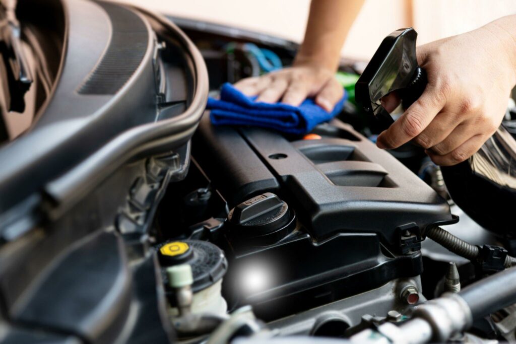 Hand of a man holding a clean spray cleaner and microfiber towel cleaning the engine bay of the car.