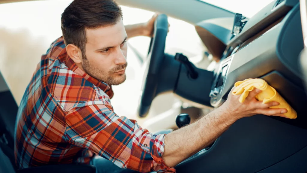 Man cleaning car's interior plastic with yellow microfiber towel.