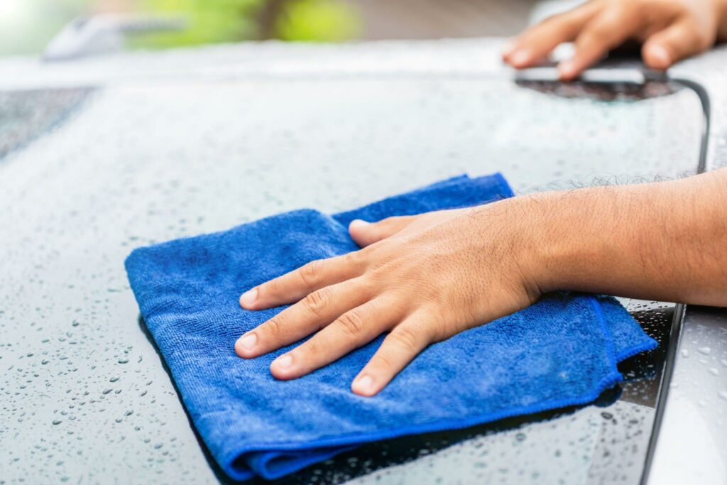 Man drying a car using blue microfiber towel.