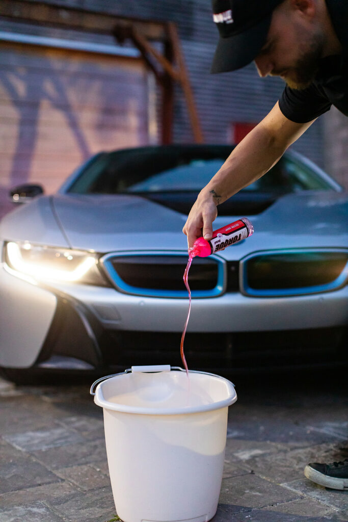 Man adding Torque Detail Decon Soap to the bucket of water.