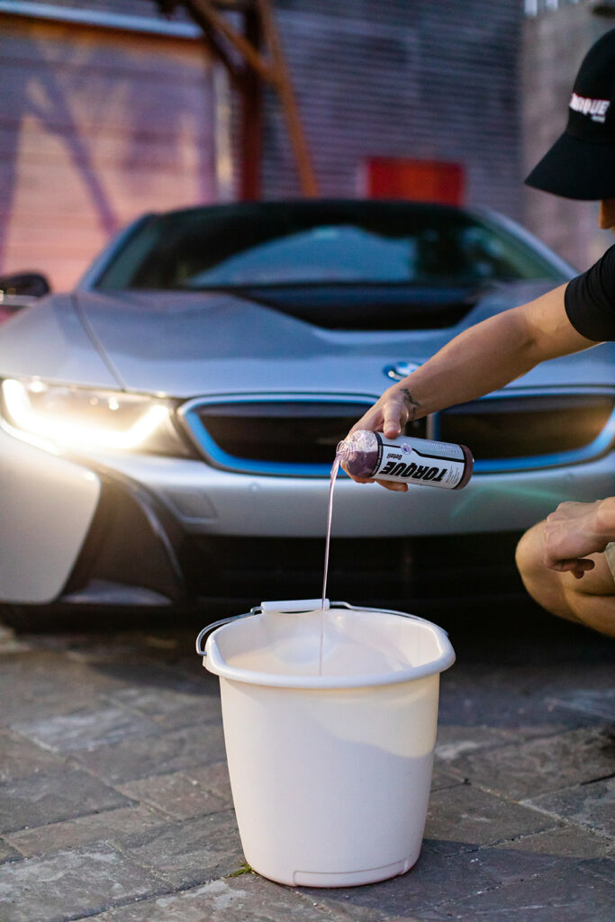 Man adding Torque Detail Ceramic Car Shampoo to the bucket of water.