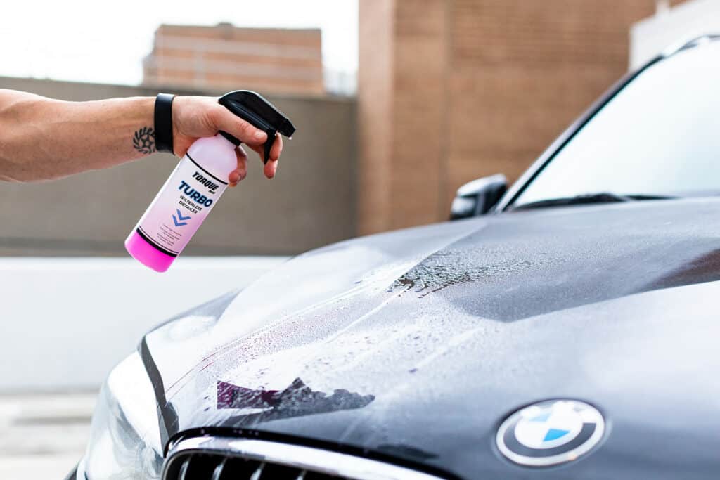 Holding Torque Detail Turbo Waterless Detailer in front of the car's bonnet.