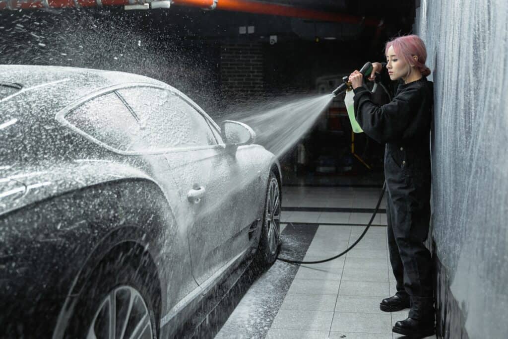 Girl pressure washing exterior of the black car.