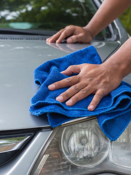 Cleaning a car with a blue microfiber towel.